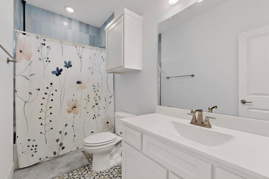 Bathroom featuring patterned floor tiling, a white vanity with integrated sink, and an overhead storage cabinet Bathroom featuring patterned floor tiling, a white vanity with integrated sink, and an overhead storage cabinet