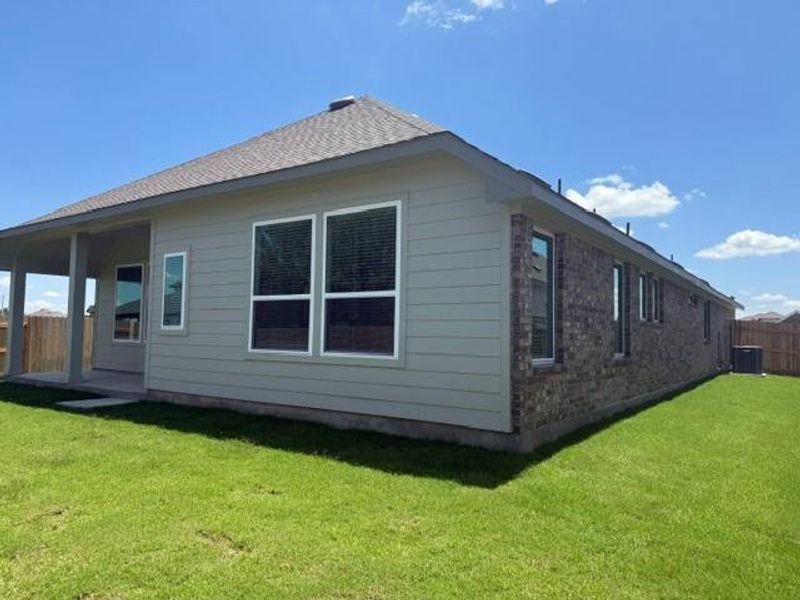 Expansive rear exterior featuring a covered patio, a spacious green lawn, light gray horizontal siding, and a brown brick facade