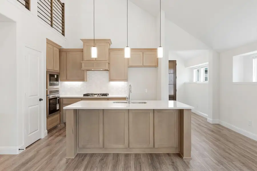 Kitchen with light wood cabinets, large island with sink, vaulted ceiling, and pendant lights over hardwood floors