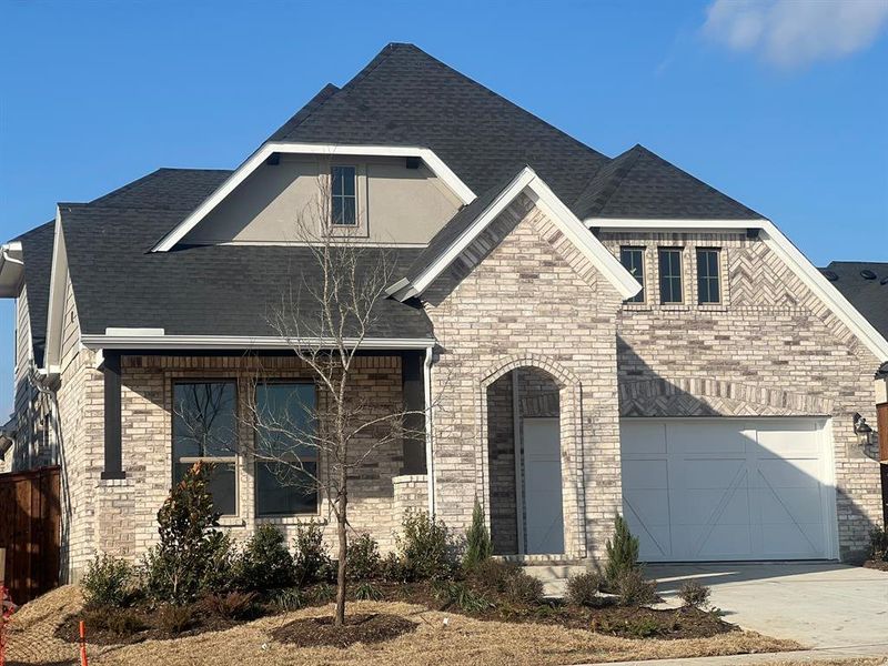 French country home with roof with shingles, concrete driveway, and brick siding