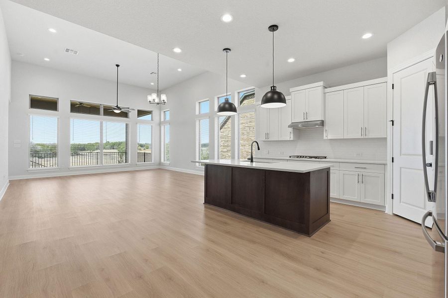 Kitchen with dual tone cabinetry, a center island with sink, stainless steel refrigerator, open floor plan, and decorative backsplash