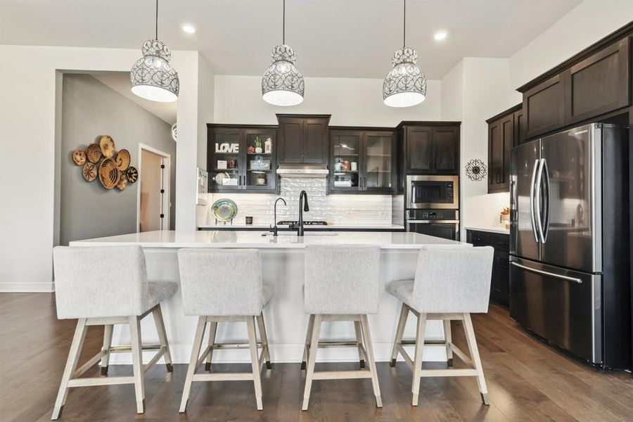 Kitchen with glass insert cabinets, appliances with stainless steel finishes, a kitchen bar, a center island with sink, and tasteful backsplash Kitchen with glass insert cabinets, appliances with stainless steel finishes, a kitchen bar, a center island with sink, and tasteful backsplash