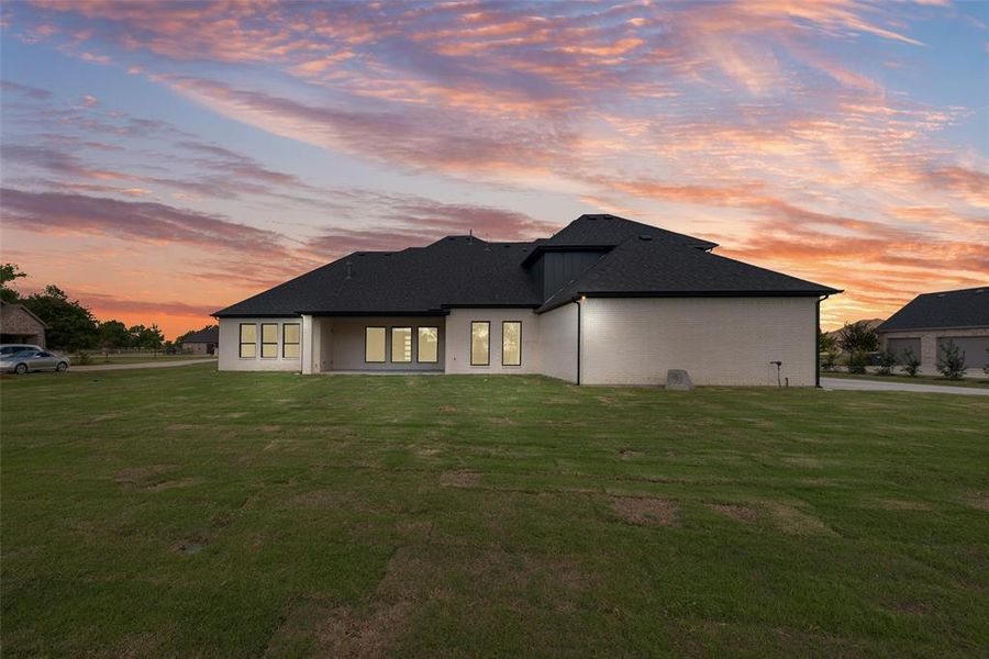 View of front of house featuring a patio area, a yard, and roof with shingles