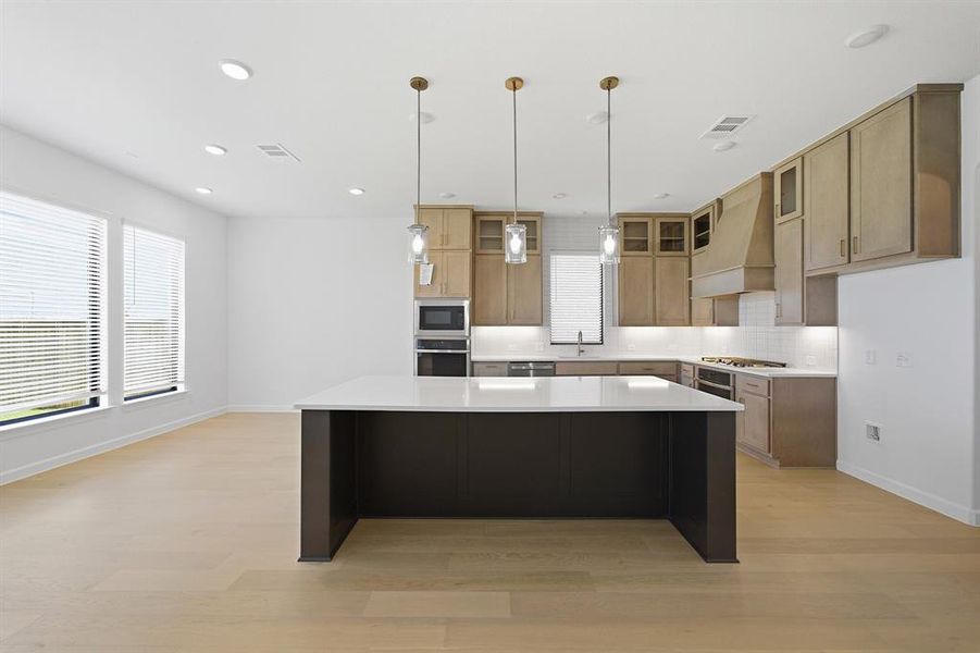 Open-concept kitchen featuring light-toned cabinetry, a large dark-toned kitchen island with a white countertop, and integrated stainless steel appliances Open-concept kitchen featuring light-toned cabinetry, a large dark-toned kitchen island with a white countertop, and integrated stainless steel appliances