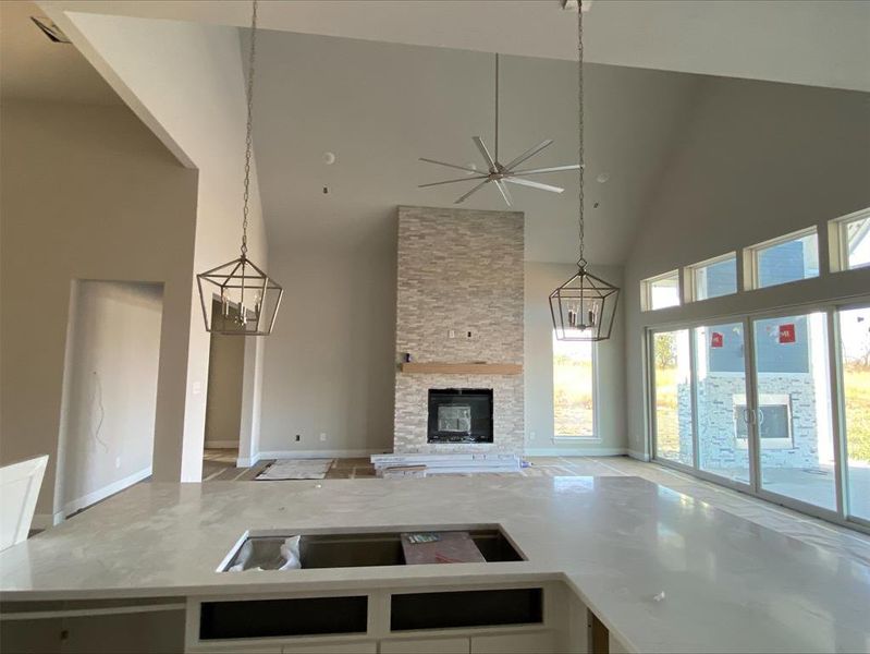 Kitchen with light stone countertops, a chandelier, ceiling fan, high vaulted ceiling, and a stone fireplace Kitchen with light stone countertops, a chandelier, ceiling fan, high vaulted ceiling, and a stone fireplace