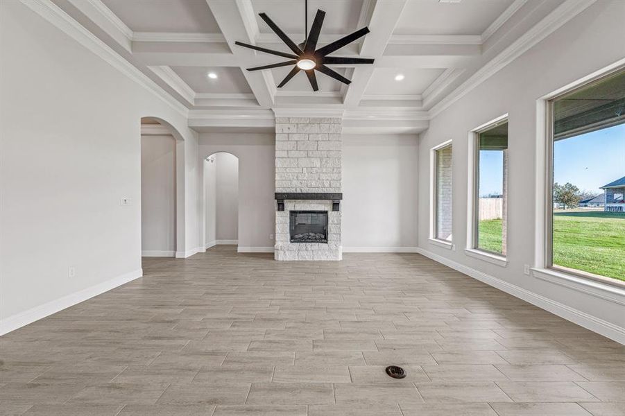 Unfurnished living room with beamed ceiling, arched walkways, wood tiled floors, coffered ceiling, and a large fireplace