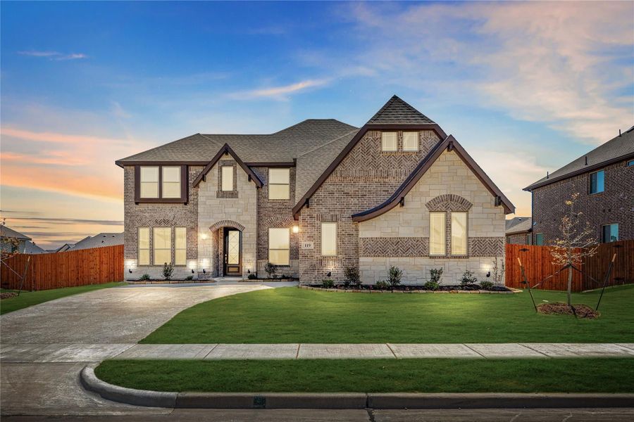 Two-story brick and stone home with arched entry, large windows, and manicured front lawn at dusk Two-story brick and stone home with arched entry, large windows, and manicured front lawn at dusk