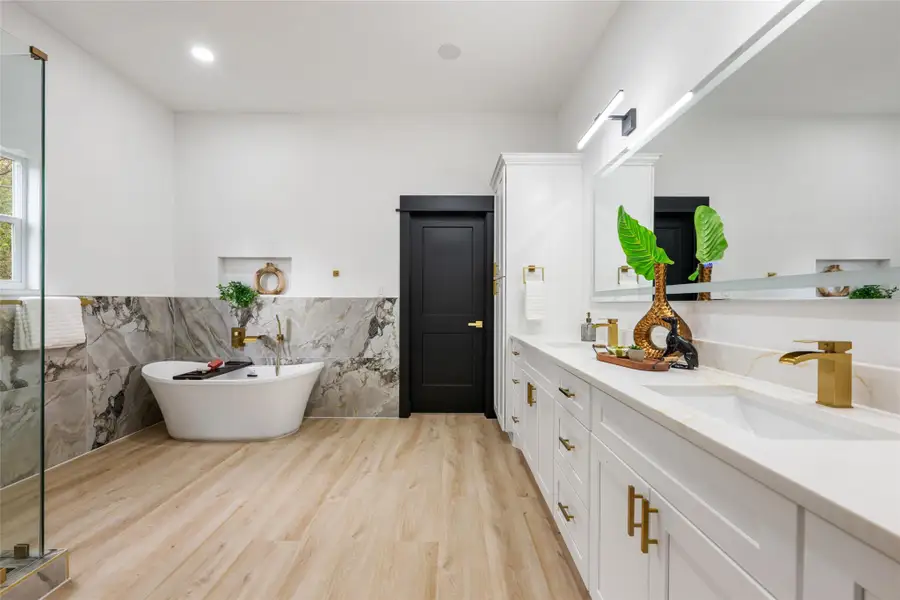Full bath featuring double vanity, a freestanding bath, a wainscoted wall, tile walls, and light wood-style floors Full bath featuring double vanity, a freestanding bath, a wainscoted wall, tile walls, and light wood-style floors
