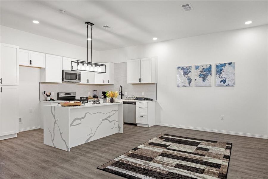 Kitchen with hardwood / wood-style flooring, appliances with stainless steel finishes, white cabinetry, a kitchen island, and decorative light fixtures