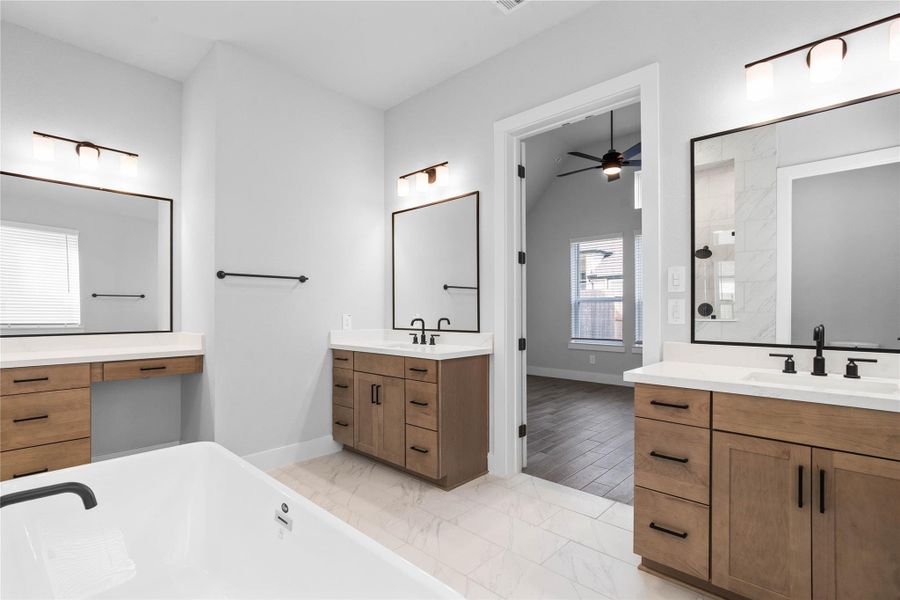 This stunningly updated primary bathroom is truly move-in ready! It features gorgeous dual vanity cabinetry with light countertops, large framed mirrors, soaring ceilings, custom paint, and sleek modern fixtures. The thoughtful layout includes a dedicated makeup vanity, offering a private and well-lit space for morning routines.