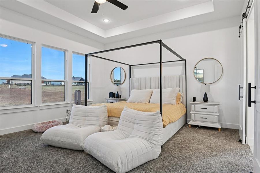 Carpeted bedroom featuring a tray ceiling, a barn door, ceiling fan and recessed lighting Carpeted bedroom featuring a tray ceiling, a barn door, ceiling fan and recessed lighting