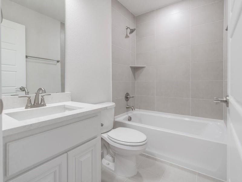 Full bathroom featuring tiled shower / bath, vanity, toilet, and tile patterned flooring