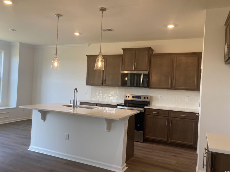 Kitchen with appliances with stainless steel finishes, decorative backsplash, a breakfast bar, decorative light fixtures, and recessed lighting