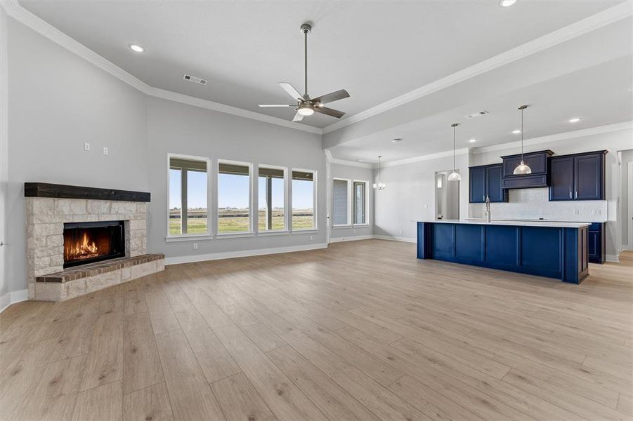 Unfurnished living room with a stone fireplace, crown molding, ceiling fan, light wood finished floors, and recessed lighting