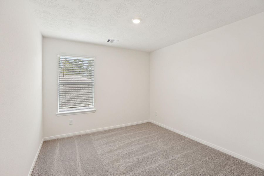 Secondary bedroom features plush carpet, neutral paint, lighting, large windows with privacy blinds, and a walk-in closet.