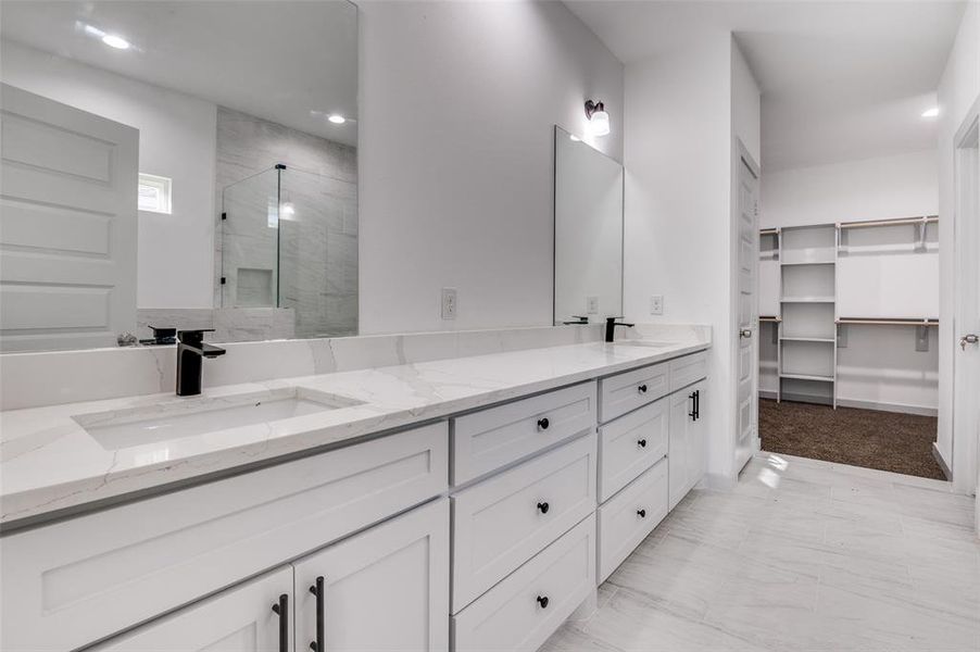 Full bathroom with double vanity, a shower stall, a walk in closet, and a sink