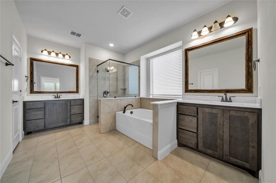 Bathroom featuring two vanities, light tile patterned floors, a stall shower, and a garden tub Bathroom featuring two vanities, light tile patterned floors, a stall shower, and a garden tub