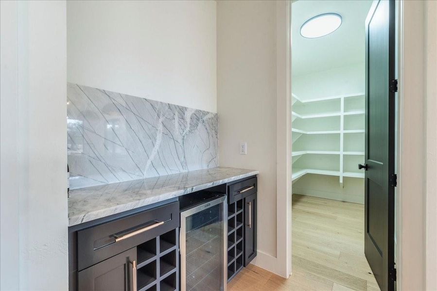 The wine bar, featuring Aurora Borealis quartzite and a mini refrigerator, is conveniently located off the kitchen for easy access to your favorite beverages.