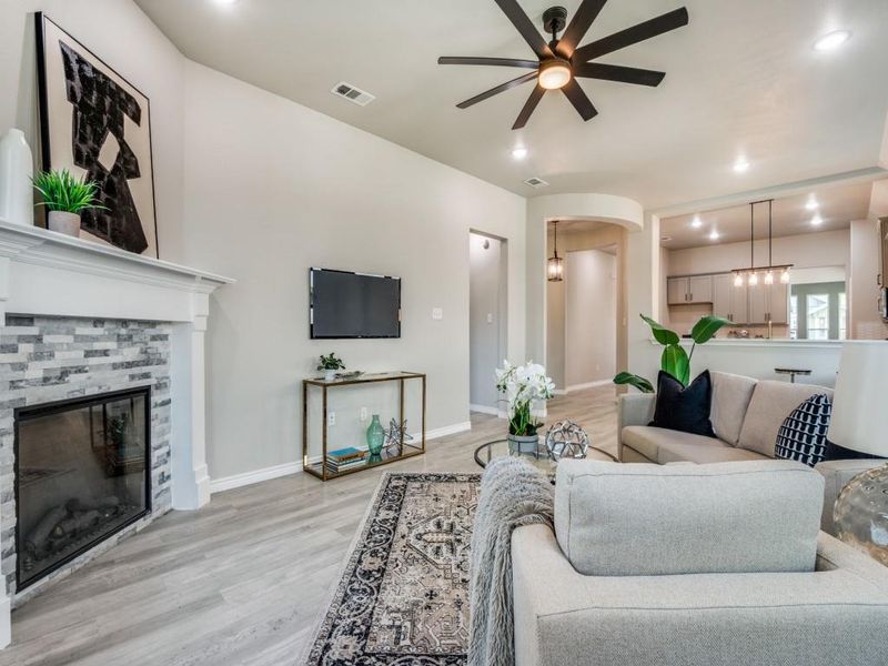 Living area featuring visible vents, arched walkways, ceiling fan, light wood-style flooring, and a tile fireplace Living area featuring visible vents, arched walkways, ceiling fan, light wood-style flooring, and a tile fireplace