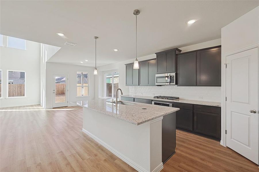 Kitchen with pendant lighting, an island with sink, light wood-type flooring, light stone counters, and decorative backsplash