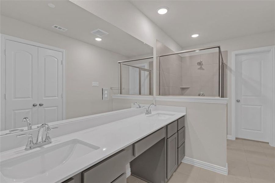 Featuring a long double vanity with ample storage, a large mirror, and a separate shower with glass enclosure.