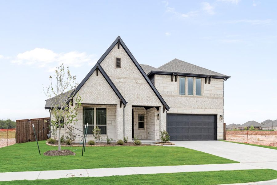Two-story home with light stone exterior, dark trim, two-car garage, and green front lawn