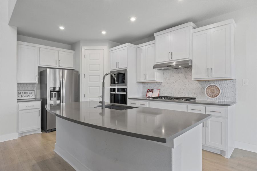 Modern kitchen with sleek white cabinetry, stainless steel appliances, and a spacious island featuring a sink and ample counter space.
