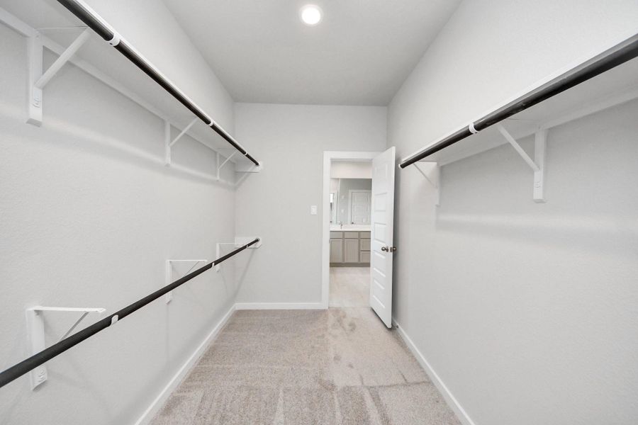 Walk-in closet that epitomizes luxury and practicality. This generously sized space features built-in shelving, offering abundant room for impeccable organization. High ceilings and recessed lighting create a bright and welcoming ambiance. Sample photo of completed home with similar floor plan. Actual colors and selections may vary.