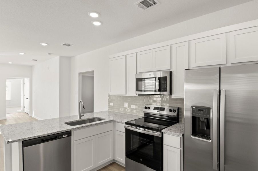 Kitchen with stainless steel appliances, a peninsula, white cabinets, light stone countertops, and recessed lighting