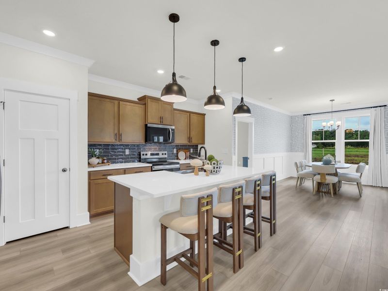 Kitchen with brown cabinetry, wainscoting, a kitchen bar, hanging light fixtures, and stainless steel appliances