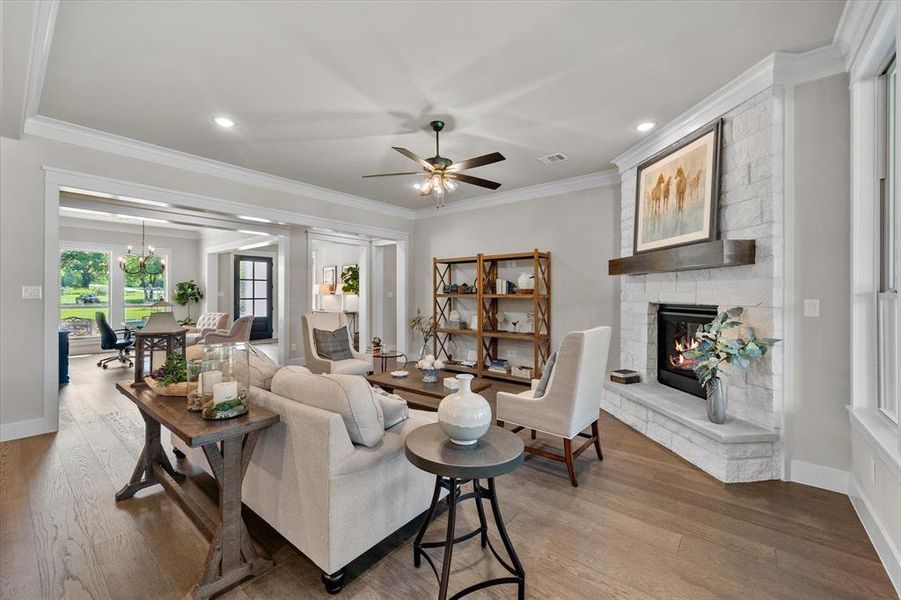 Living room featuring ceiling fan, a large fireplace, crown molding, and floors!