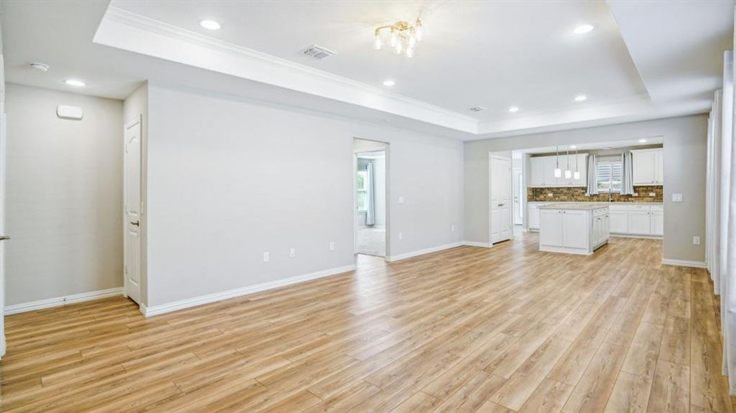 Unfurnished living room featuring a raised ceiling, recessed lighting, plenty of natural light, light wood-style flooring, and ornamental molding Unfurnished living room featuring a raised ceiling, recessed lighting, plenty of natural light, light wood-style flooring, and ornamental molding