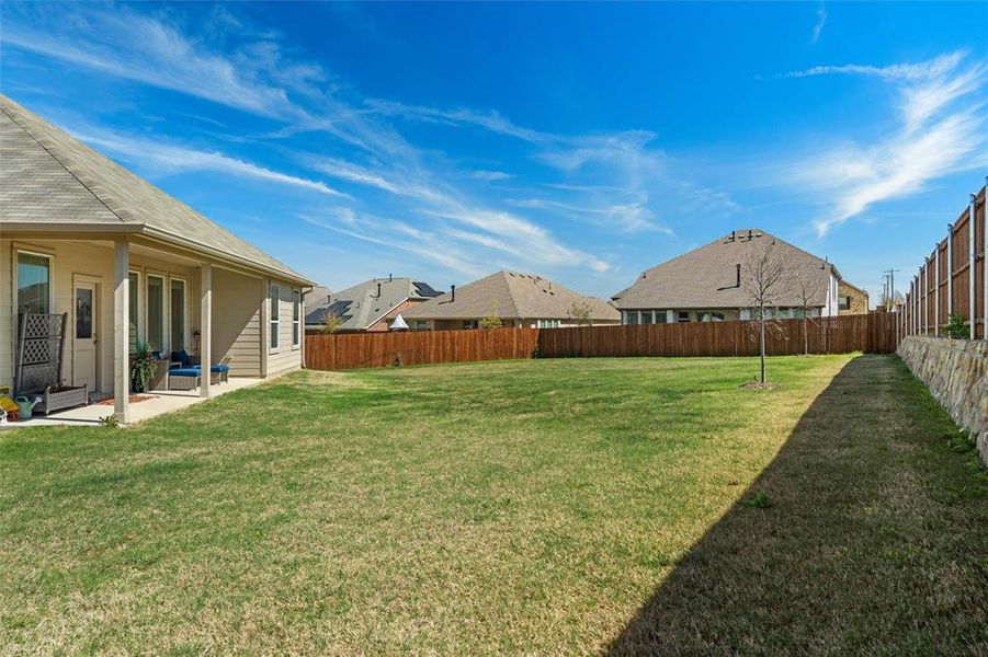 Spacious lawn with a covered patio, multiple windows, and a wood privacy fence