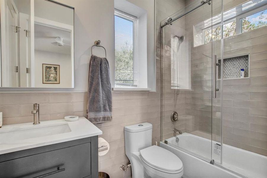 Bathroom featuring bath / shower combo with glass door, vanity, healthy amount of natural light, and tile walls