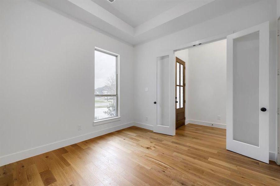This room features light-colored hardwood flooring, a window with a view of the outdoors, and a recessed ceiling