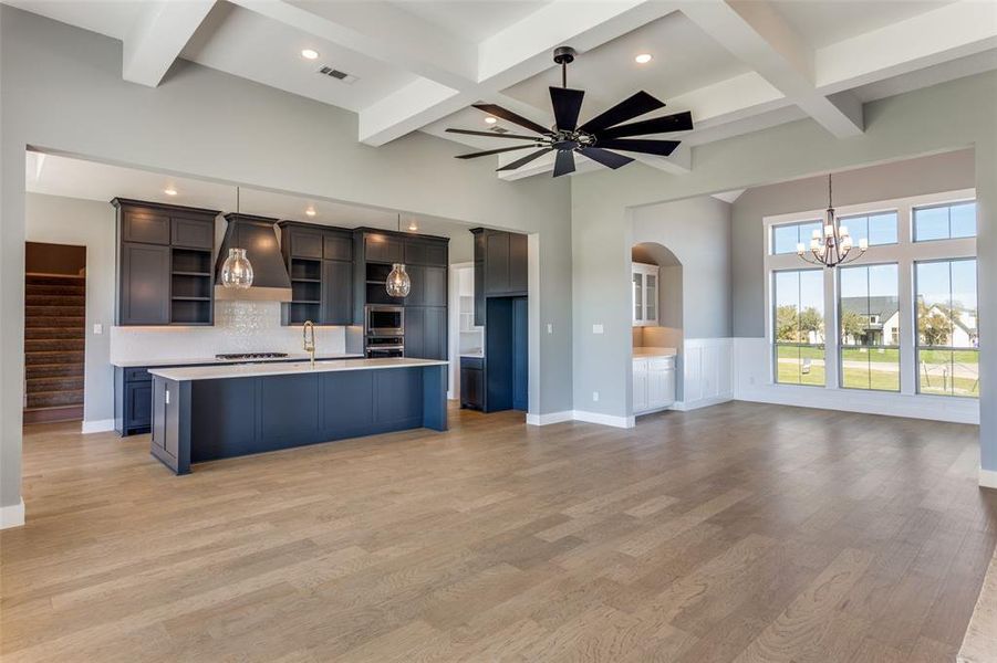 Kitchen featuring an island with sink, open shelves, open floor plan, beam ceiling, and light wood-style flooring Kitchen featuring an island with sink, open shelves, open floor plan, beam ceiling, and light wood-style flooring