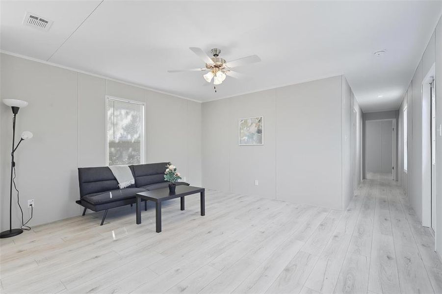 Living area with light wood-style floors, ornamental molding, a decorative wall, and ceiling fan Living area with light wood-style floors, ornamental molding, a decorative wall, and ceiling fan