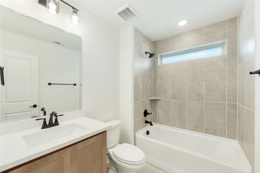 Bathroom with single vanity, white tub, and tiled shower surround with black fixtures