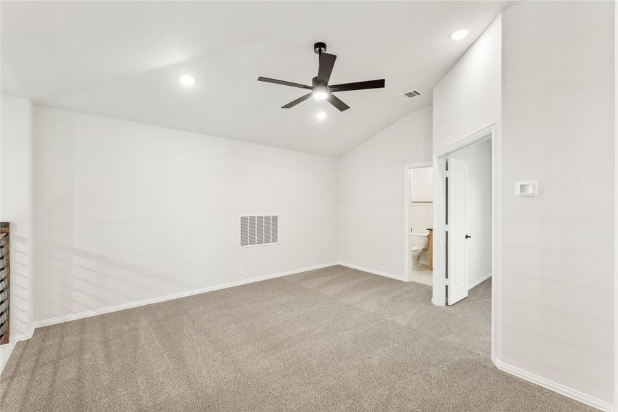 Empty bedroom with vaulted ceiling, ceiling fan, carpet flooring, and ensuite bathroom door Empty bedroom with vaulted ceiling, ceiling fan, carpet flooring, and ensuite bathroom door