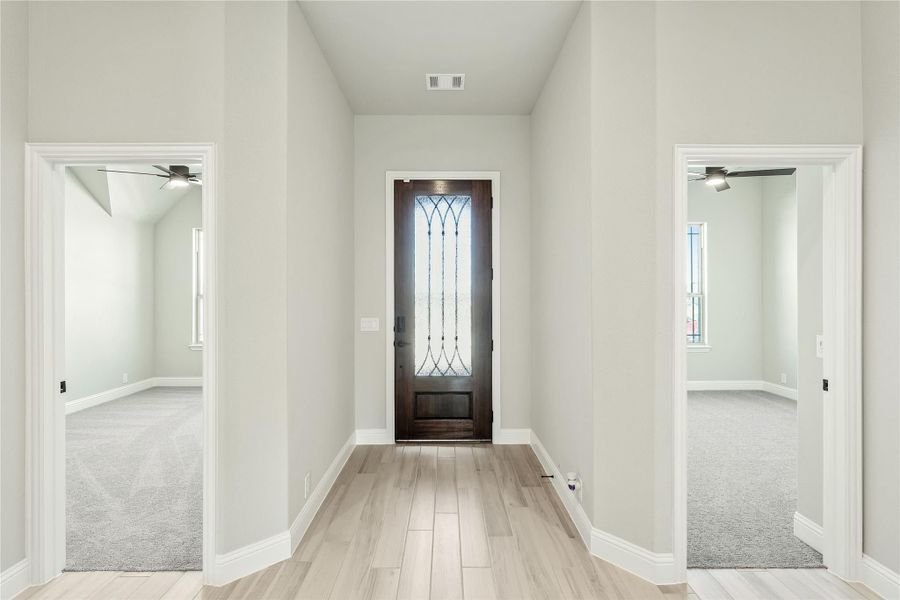 Entryway hallway with dark wood front door featuring decorative glass, light wood floors, and two open rooms on each side Entryway hallway with dark wood front door featuring decorative glass, light wood floors, and two open rooms on each side