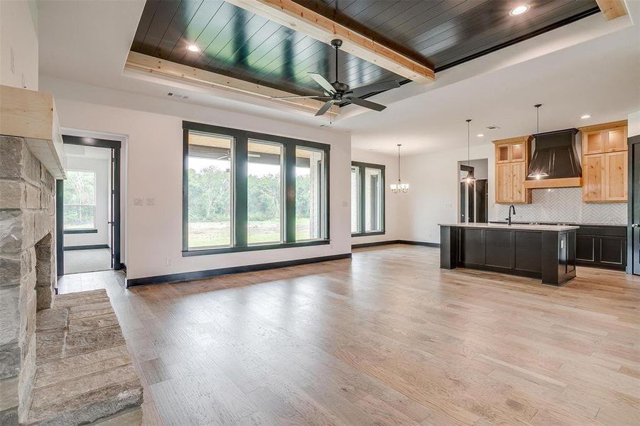 Unfurnished living room with a tray ceiling, beam ceiling, a fireplace, and light hardwood / wood-style flooring