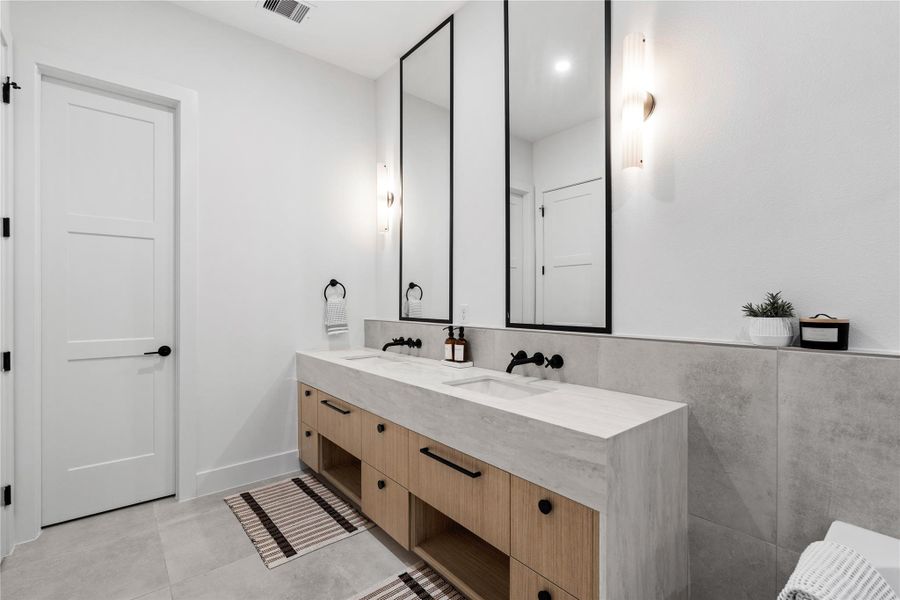 Natural wood tones soften the modern silhouette of this dual-sink vanity, where statement mirrors and matte fixtures create a gallery-like finish.