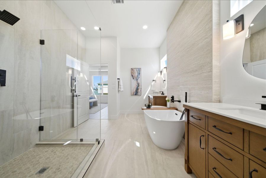 This bathroom features a modern design with a spacious glass-enclosed shower, a freestanding bathtub, and a double vanity with wooden cabinetry. The room is bright and airy, with neutral tones and stylish lighting.