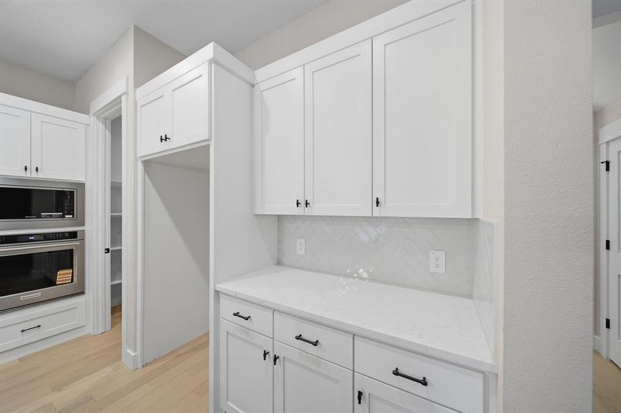 Kitchen with white cabinets, appliances with stainless steel finishes, light stone countertops, light wood-style floors, and backsplash Kitchen with white cabinets, appliances with stainless steel finishes, light stone countertops, light wood-style floors, and backsplash