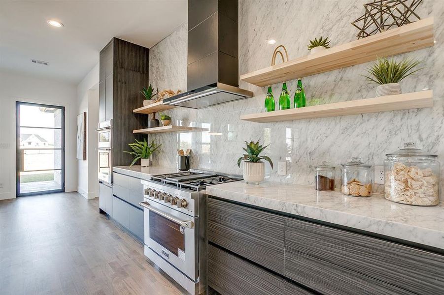 Kitchen with open shelves, modern cabinets, appliances with stainless steel finishes, light stone countertops, and custom exhaust hood Kitchen with open shelves, modern cabinets, appliances with stainless steel finishes, light stone countertops, and custom exhaust hood