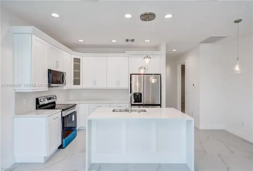 Kitchen featuring white shaker-style cabinetry, a central island with a solid-surface countertop, stainless steel appliances, and tile flooring