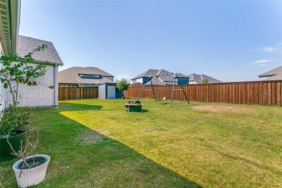 Fenced backyard with a storage shed, a fire pit, and a playground