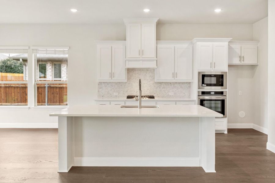 White kitchen with large island, quartz countertops, marble backsplash, and stainless steel double wall ovens