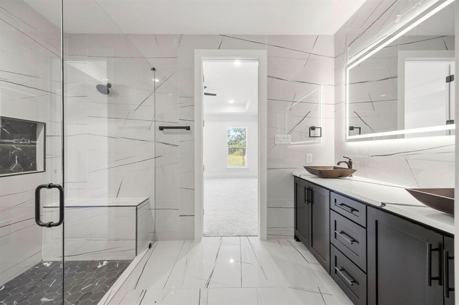 Spacious bathroom featuring a glass-enclosed shower with bench seating, dual dark wood-finish vanities, vessel sinks, an illuminated mirror, and large format tiled flooring Spacious bathroom featuring a glass-enclosed shower with bench seating, dual dark wood-finish vanities, vessel sinks, an illuminated mirror, and large format tiled flooring