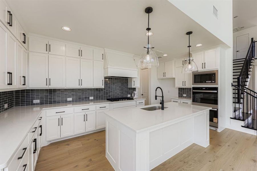 Kitchen with a center island with sink, decorative backsplash, decorative light fixtures, white cabinets, and light wood-style flooring